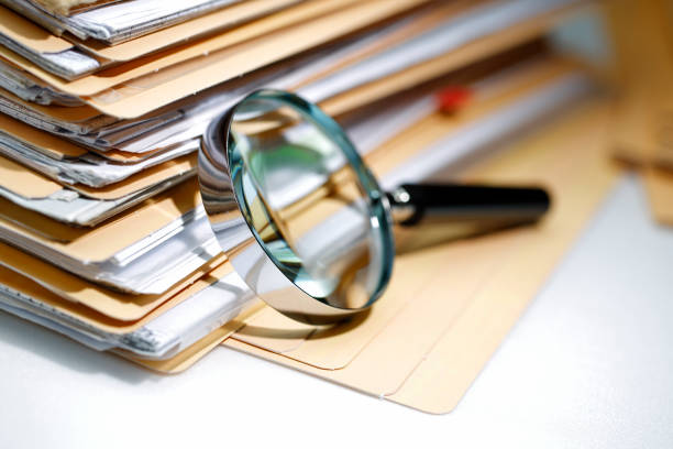 A magnifying glass lying next to a stack of file folders